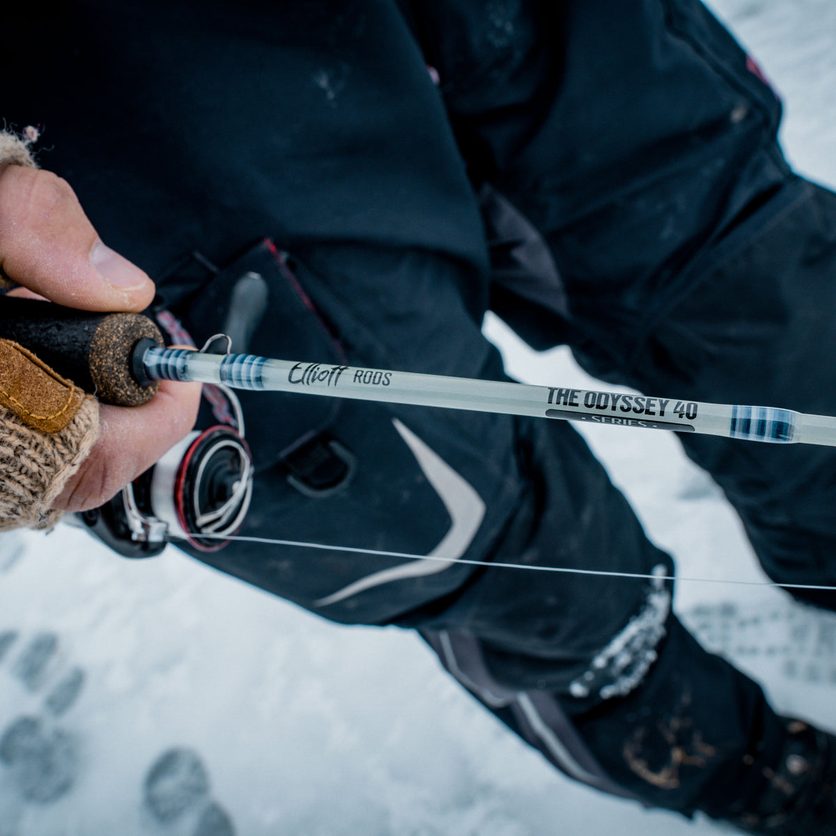 Person holding an elliott fishing rod with 'The Odyssey' branding in a snowy landscape